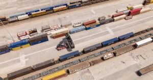 High angle drone shot of a logistics hub with stacked containers and a forklift.